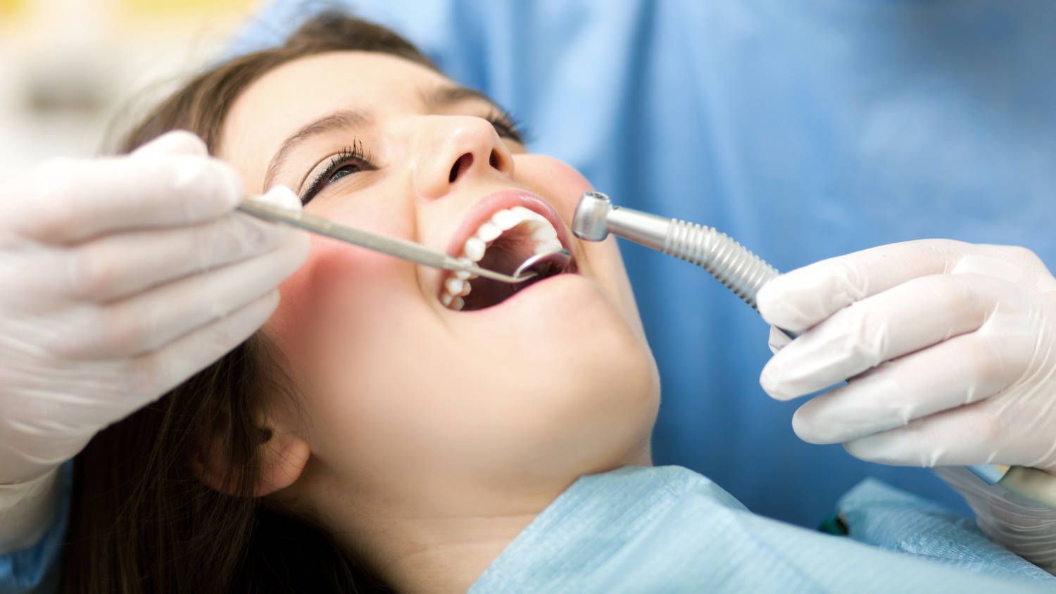 Kobieta leży z otwartą buzią na fotelu dentystycznym, a stomatolog rozpoczyna leczenie reendo, czyli zabieg powtórnego leczenia kanałowego.